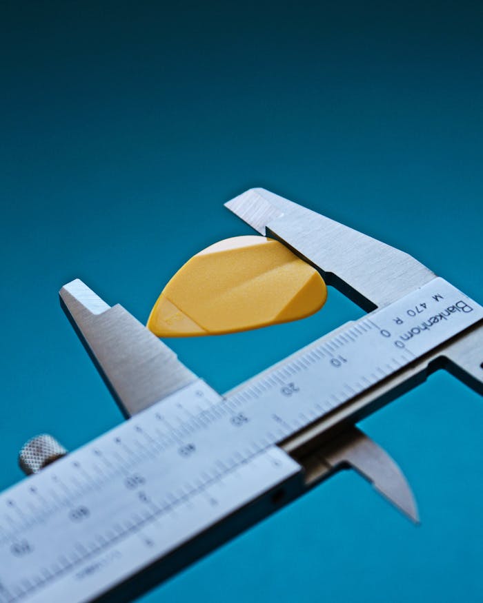 Close-up of a yellow guitar pick measured with calipers for precision.