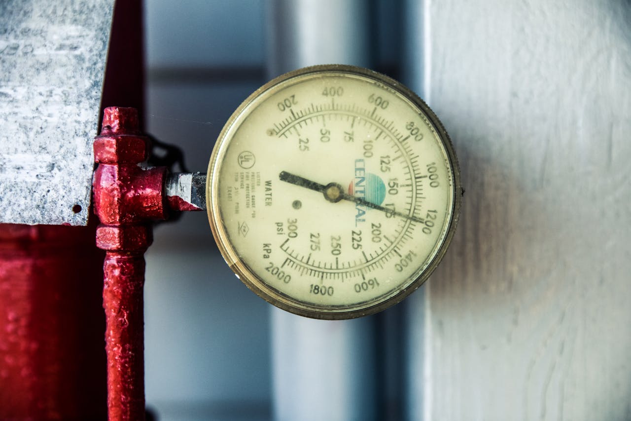 Detailed view of a pressure gauge attached to a red industrial pipe, measuring PSI and kPa.